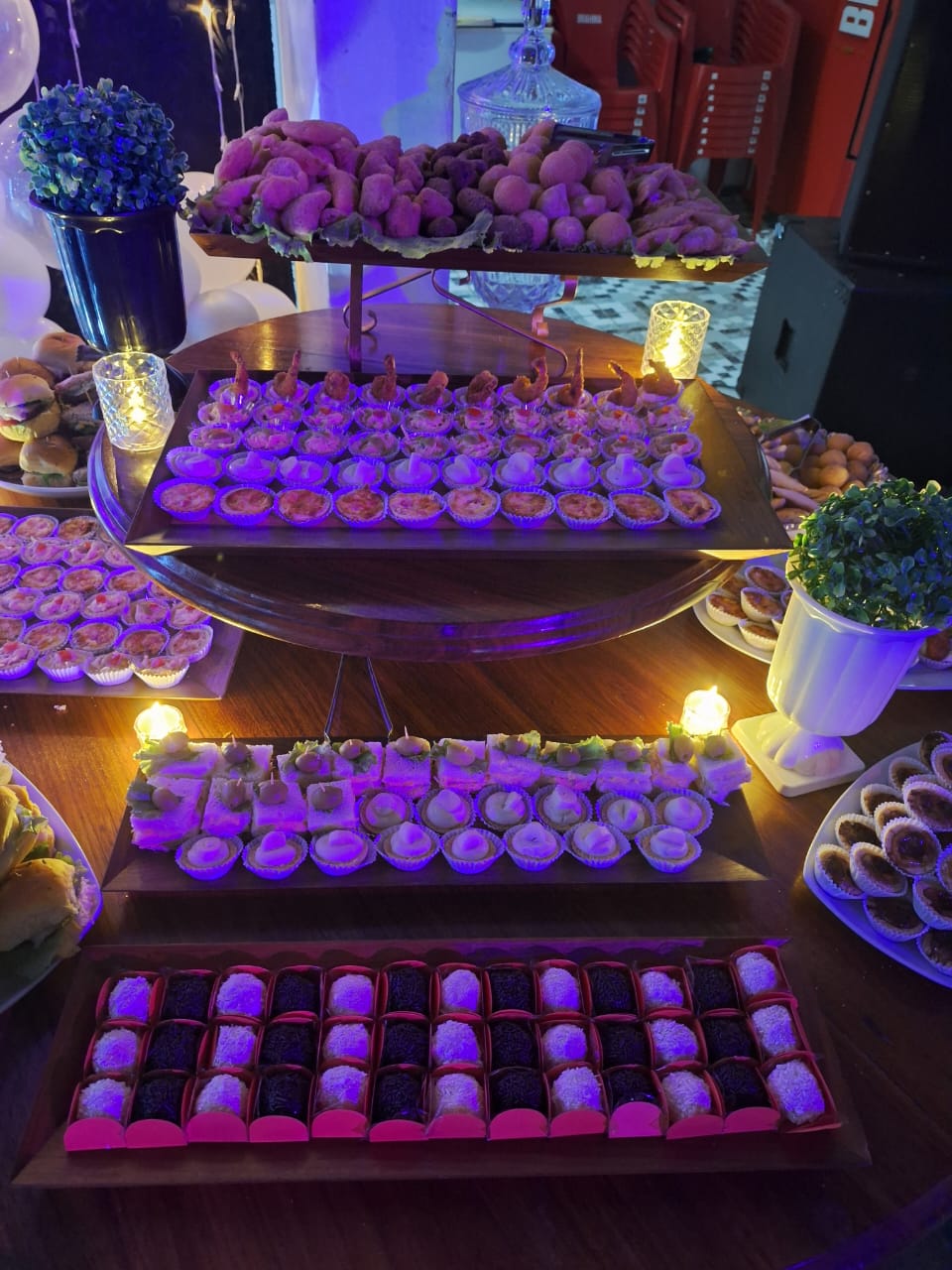 Mesa de evento com doces e salgados em iluminação roxa